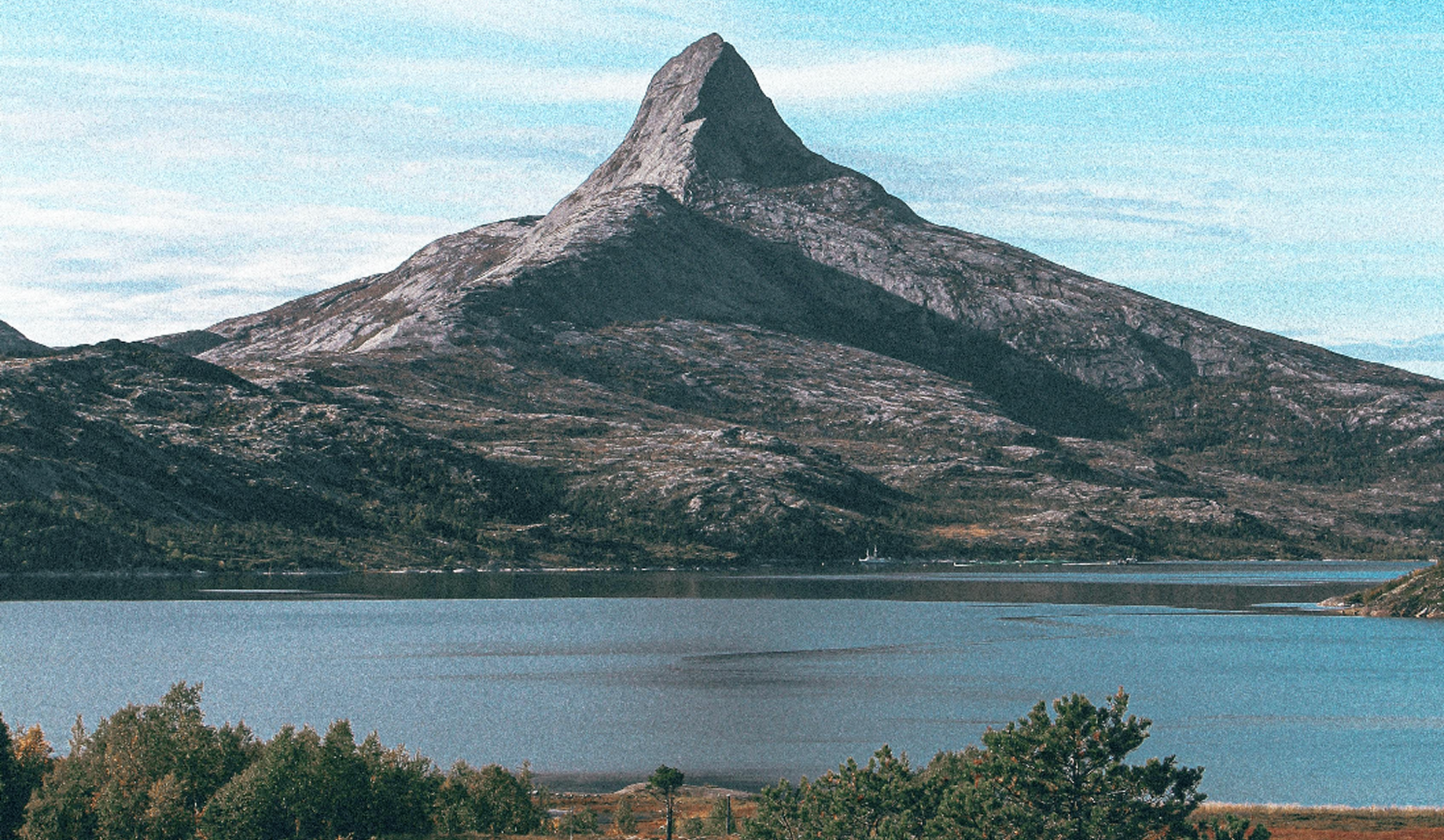 Jagged mountain peak reflected in a calm lake with blue sky above